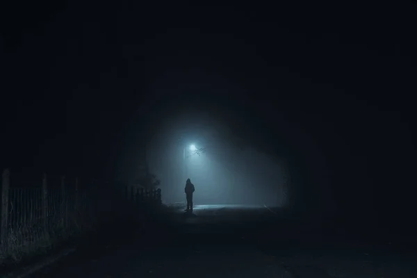 A dark scary concept of a man silhouetted against a street light on a spooky, foggy winters night