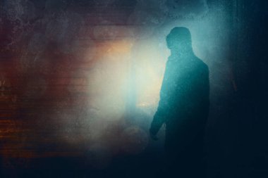 Kapüşonlu kapüşonlu bir figür, geceleri kameraya geri dönüyor. Işıklara karşı siluet. Bir neon grunge düzenleme ile