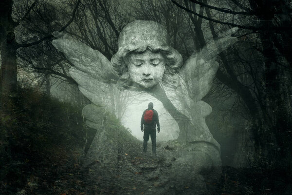 A mystery concept of a hiker lost in a spooky winters forest. With a double exposure of a graveyard angel over the top. With a grunge, vintage edit.