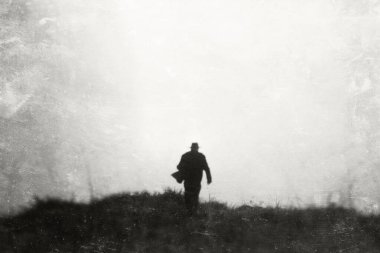 A  mysterious concept of a man wearing a hat and coat running away from the camera. With a black and white, artistic edit