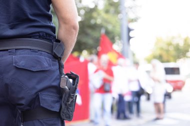 Sokak protestosu sırasında görevli polis memuru, arka planda protestocular bulanık