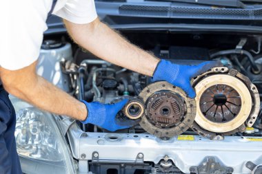 Otomotiv teknisyeninin elinde ikinci el basınçlı plaka, debriyaj diski ve aracın motorunun önündeki yatağı var.