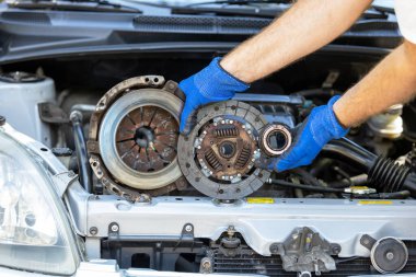 Otomotiv teknisyeninin elinde ikinci el basınçlı plaka, debriyaj diski ve aracın motorunun önündeki yatağı var.