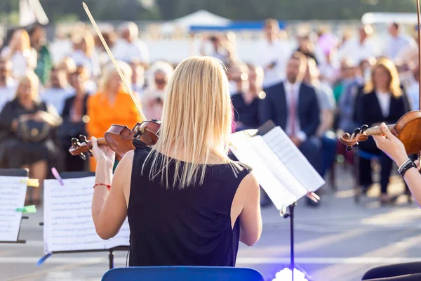 Female musician playing violin at classical music concert outdoors in front of blurred audience