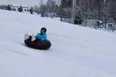 Mutlu çocuklar kar kaydırağında bir borunun üzerinde kayıyorlar. Kar altındaki çocuklar için aktif kış oyunları. Buz üstünde eğlenceli kış tatili