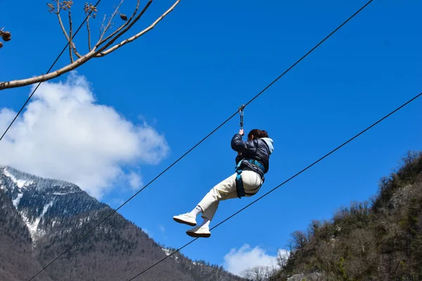 Dağlarda halatla kayma. Dağların arasındaki vadide bir ip gezisi. Bir kadın yüksek bir yerden ip üzerinde iniyor. Zirvedeki teleferik..