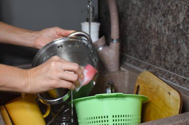 Kadın mutfaktaki lavaboda bulaşıkları yıkıyor. Ev hanımı evde bulaşıkları yıkıyor..