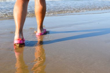 Deniz kenarındaki kumların üzerindeki ayakların yansıması. Islak kumda ayakların güneşli gölgesi