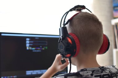 a boy with headphones sits at a computer playing online games. children's gambling addiction.