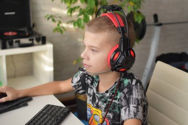 Caucasian boy in red headphones is trained at home at the computer. child playing online game