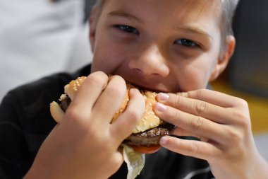 boy with appetite eats delicious hamburger. child bites off a large piece of sandwich