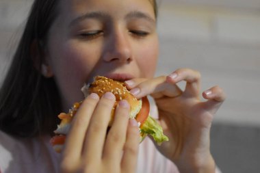 girl with appetite eats a delicious hamburger. child bites off a large piece of sandwich