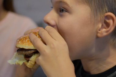 boy with appetite eats delicious hamburger. child bites off a large piece of sandwich