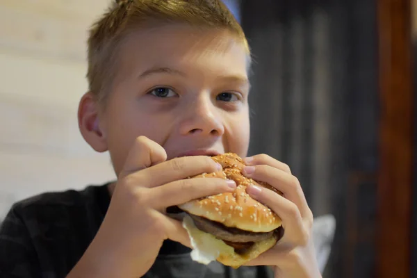 食欲のある少年はおいしいハンバーガーを食べる 子供は大きなサンドイッチを噛んで — ストック写真