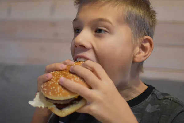 食欲のある少年はおいしいハンバーガーを食べる 子供は大きなサンドイッチを噛んで — ストック写真