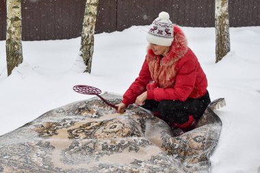 beat the carpet from dust in the winter in the snow. cleaning home carpets with snow. the carpet lies on white snow