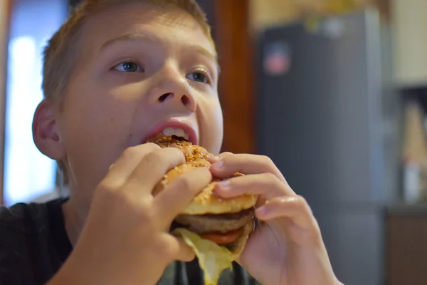 フライドポテトでおいしいファーストフードのハンバーガーを食べる少年 — ストック写真