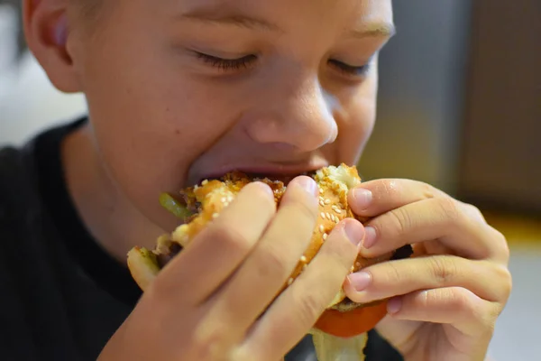 フライドポテトでおいしいファーストフードのハンバーガーを食べる少年 — ストック写真