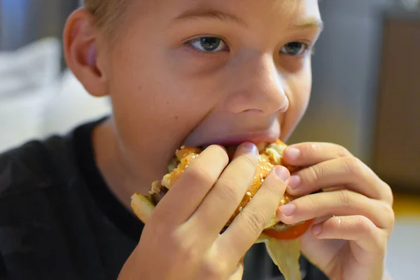 フライドポテトでおいしいファーストフードのハンバーガーを食べる少年 — ストック写真