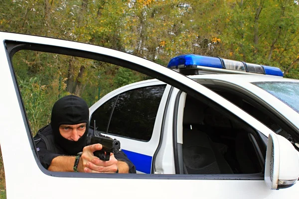 Maskovaný policista střílí z policejního auta — Stock fotografie