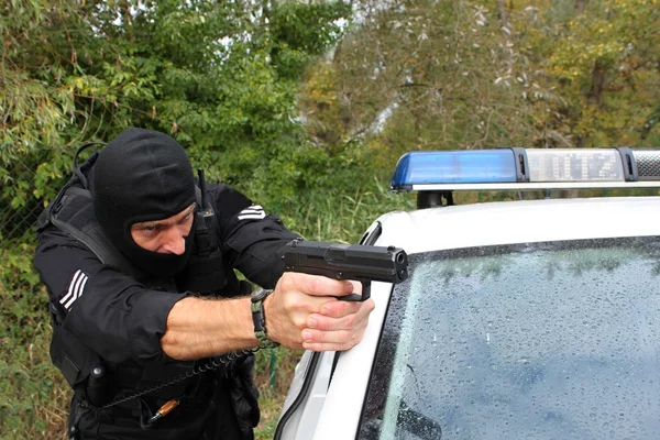 Masked policeman shoots from police car — Stock Photo, Image