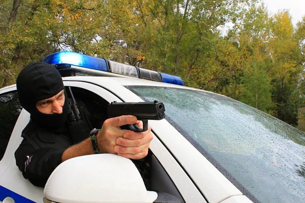 Maskovaný policista střílí z policejního auta — Stock fotografie