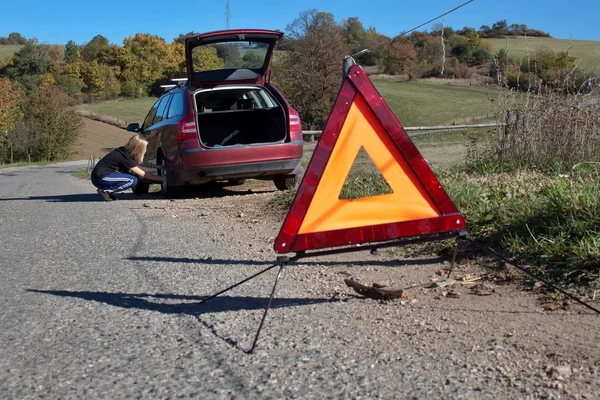 Una giovane ragazza cerca di riparare un'auto rotta su una strada deserta — Foto Stock