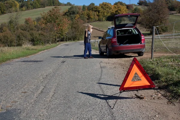 Молода дівчина намагається відремонтувати зламану машину на безлюдній дорозі — стокове фото