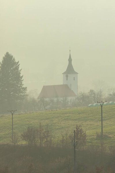 Туманный осенний день. Вид на церковь в деревне Долни-Луцкий в Чешской Республике. Церковь в тумане. Осенний туман в деревне.