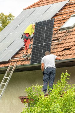 Two men installing new solar panels on the roof of a private house. Renewable energy concept. Iinstallation of photovoltaics. Energy saving.
