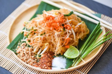 Tayland usulü kızarmış erişteli Tayland usulü karidesli fasulye filizi ve fıstıklı biber tozu limon şekeri limonlu karışık erişte Pad Thai yemek masasında servis ediliyor.