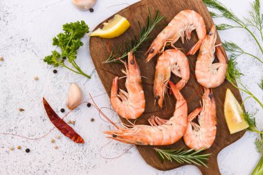 Tahta tabakta taze karides, otlar ve baharatlarla beyaz arka planda limon biberiyesi, deniz ürünleri restoranında haşlanmış karides pişirilmiş yemek.