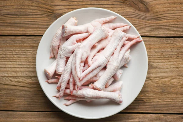 chicken feet on white plate, Fresh raw chicken feet for cooked food on the wooden table kitchen background, top view