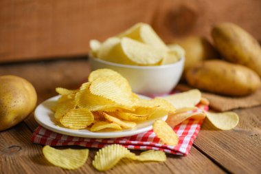 Beyaz tabakta patates cipsi, mutfak masasında patates cipsi ve taze çiğ patates.