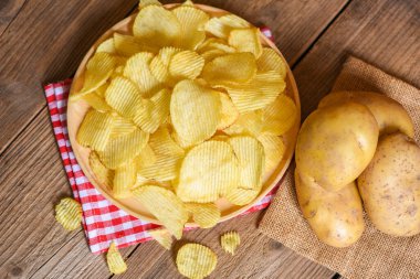 Tabak manzarasında patates cipsi, mutfak masasında patates cipsi ve taze çiğ patates.
