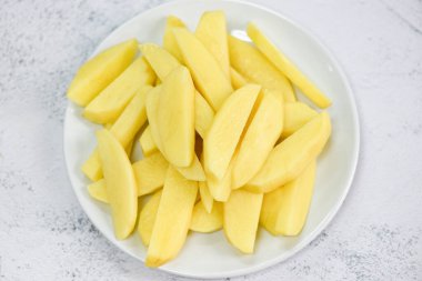 Taze çiğ patates dilimleri, beyaz tabakta pişmiş yemek için doğranmış patates.