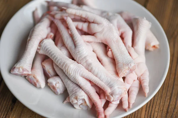 Chicken feet on white plate, Fresh raw chicken feet for cooked food on the wooden table kitchen background