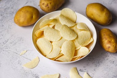 Beyaz kasede patates cipsi, mutfak masasında patates cipsi ve taze çiğ patates.