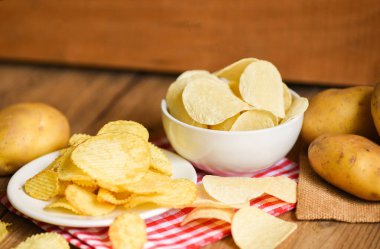 Beyaz tabakta patates cipsi, mutfak masasında patates cipsi ve ahşap zeminde taze çiğ patates. 