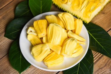 Olgun meyve kabuğu soyulmuş tropikal meyve, kaya meyvesi ağacından taze taze taze, beyaz tabakta meyve ve ahşap arka planda yaprak.