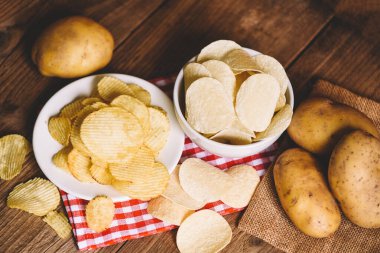 Kase ve tabakta patates cipsi, mutfak masasında patates cipsi ve tahta zeminde taze çiğ patates.