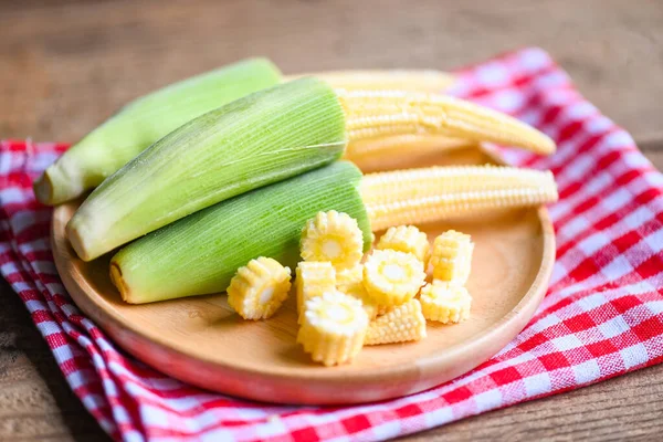 Tahta tabakta bebek mısırı, sağlıklı yemek pişirmek için taze taze taze mısır masa örtüsünün arkasında çiğ organik mısır..