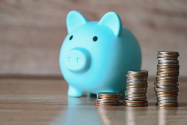 Stack coins and piggy bank on wooden background, blue piggy bank saving money for education study or investment concept