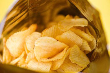 Patates cipsi naylona sarılı pakette atıştırmalık ve yemeye hazır yağ ve abur cubur, sarı arka planda patates cipsi.
