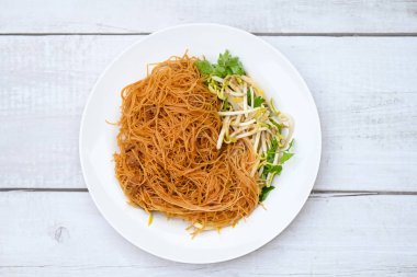 Beyaz tabakta kızarmış şehriye, fasulye filizi ve ahşap masada kişniş Çin usulü kızarmış şehriye.