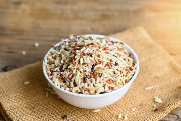 brown rice on white bowl wooden background , raw various rice color mixed thai rice for cooking food , Loonzain rice brown black red white purple health food.