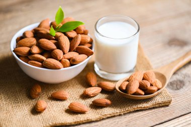 Almond milk and Almonds nuts on white bowl with green leaf on sack background, Delicious sweet almonds on the wooden table , roasted almond nut for healthy food and snack