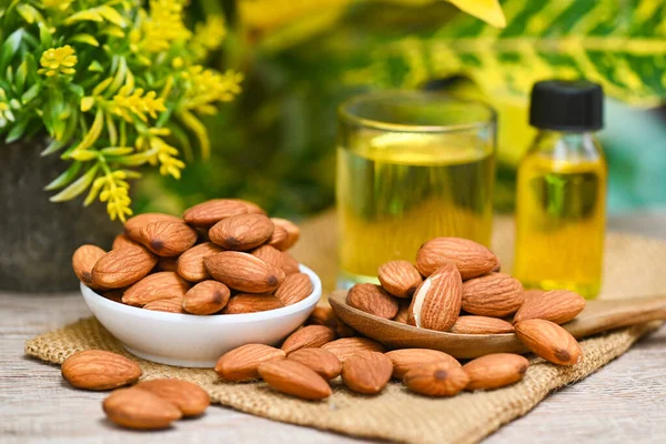 Almond oil and Almonds nuts on bowl plant green nature background, Delicious sweet almonds oil in glass bottle, roasted almond nut for healthy food and snack organic vegetable oils for cooking or spa