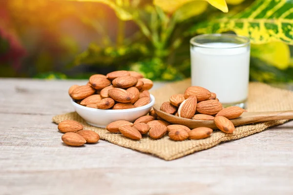 Almond milk and Almonds nuts on white bowl with green leaf on sack background, Delicious sweet almonds on the wooden table , roasted almond nut for healthy food and snack