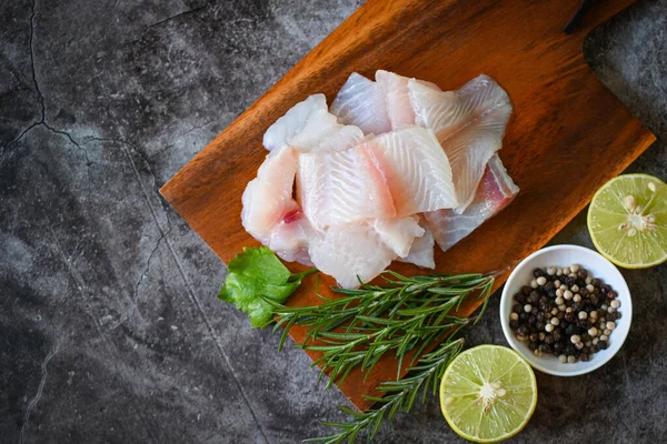 fish fillet on wooden board with ingredients for cooking, fresh raw pangasius fish fillet with herb and spices black pepper lemon lime and rosemary, meat dolly fish tilapia striped catfish - top view